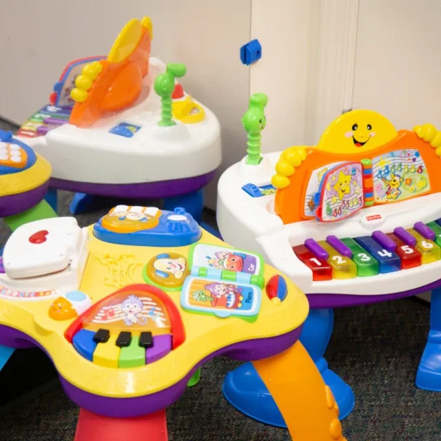 Colorful baby activity tables with buttons and piano keys, reflected in a nearby mirror.