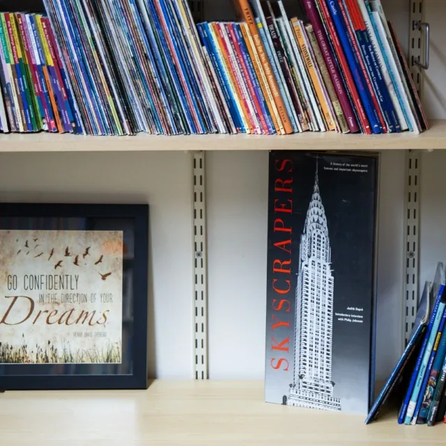 Books on shelves, a framed quote, and a tall book titled Skyscrapers with a building photo.