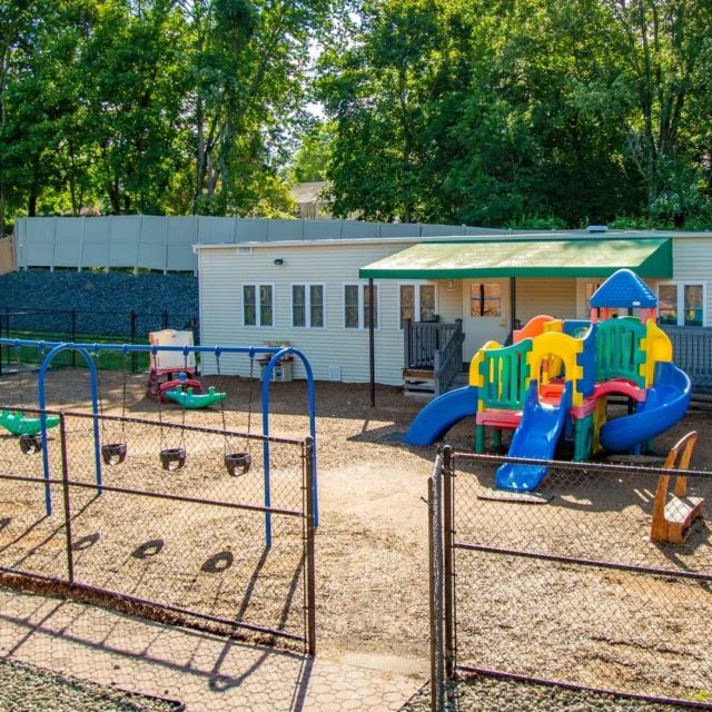 Outdoor playground with colorful slides, swings, and a small building in the background.