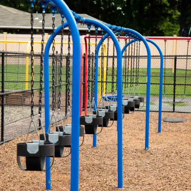 Empty black toddler swings on a blue swing set at a playground with wood chip ground covering.