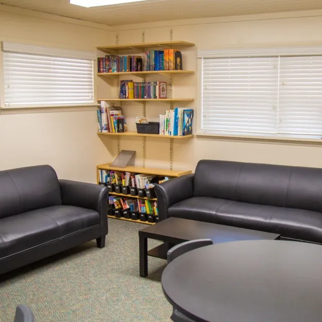 Two black sofas and bookshelves in a cozy room with windows and a small black coffee table.