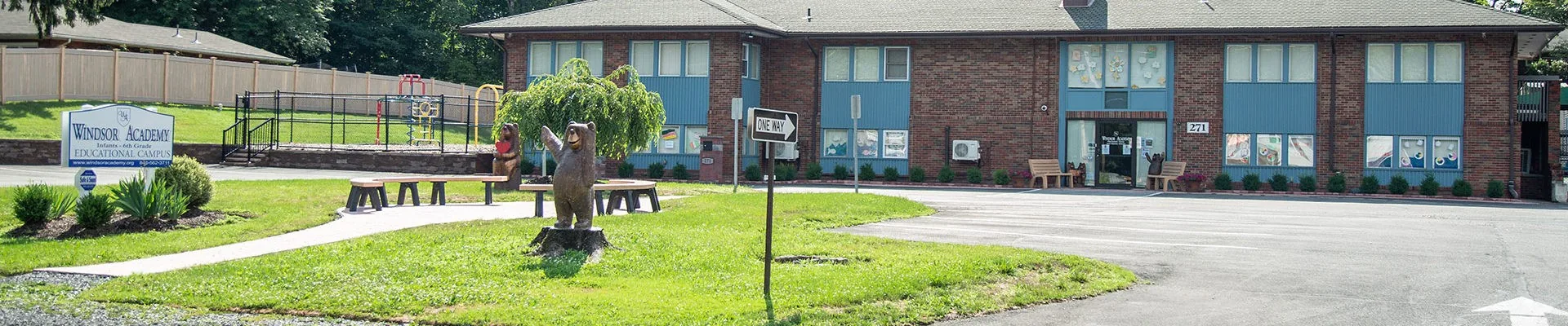 Brick building with playground, benches, bear statue, and school sign on a grassy area.