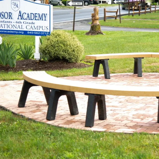 Curved benches on a brick patio near a Windsor Academy sign and green shrubs.