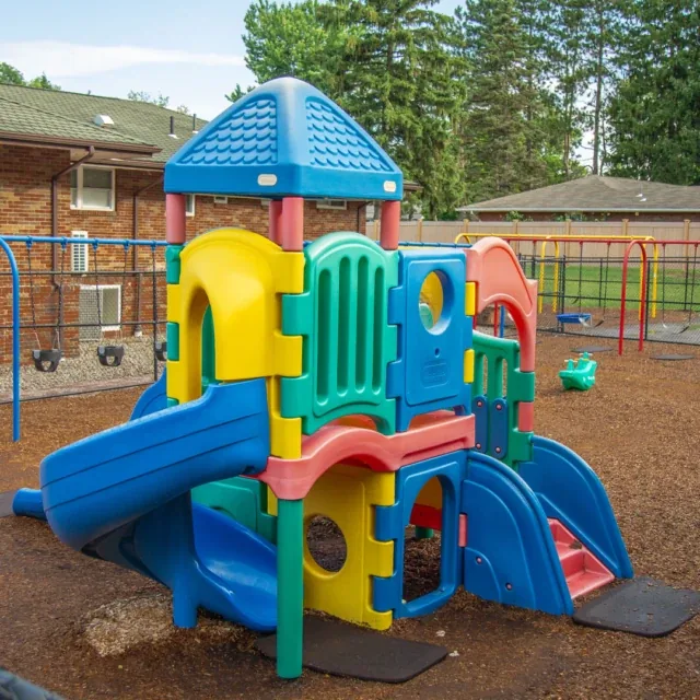 Colorful plastic playground structure with slides and tunnels in an outdoor play area.