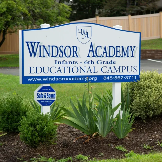 A Windsor Academy educational campus sign surrounded by greenery and bushes.
