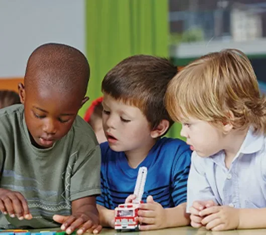 Three young boys sitting together, playing with colorful building blocks at a table.