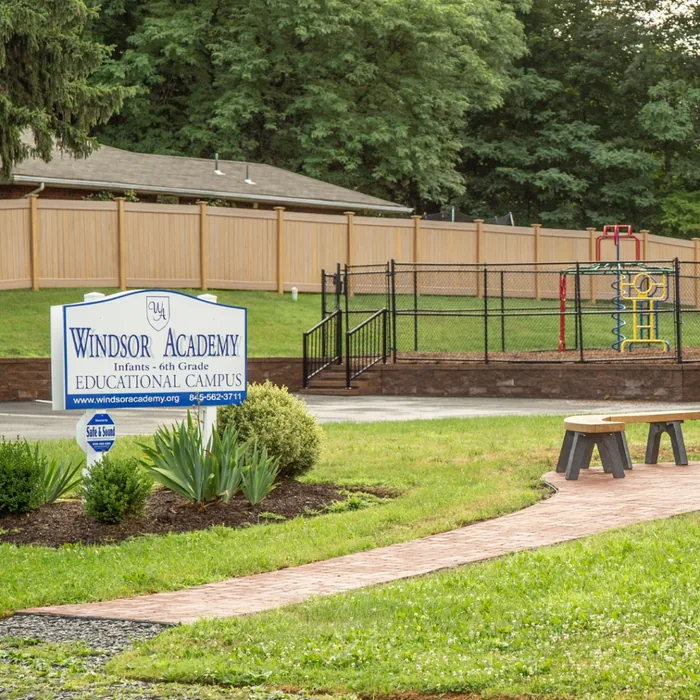 Outdoor sign for Windsor Academy in front of a playground with benches and landscaping.