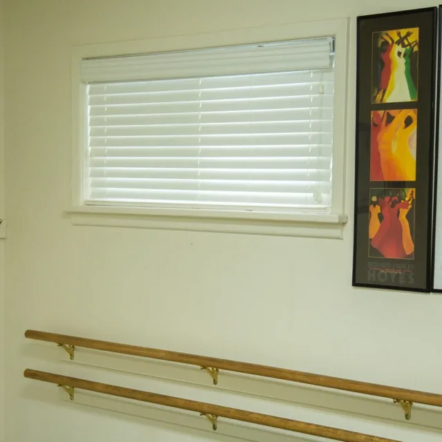 A window with closed blinds, wall art, and two wooden ballet barres mounted on the wall.