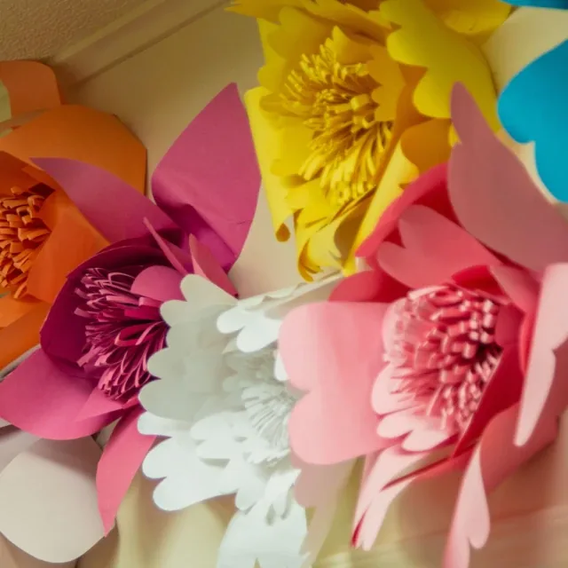 Colorful paper flowers in pink, yellow, white, orange, and blue attached to a wall.