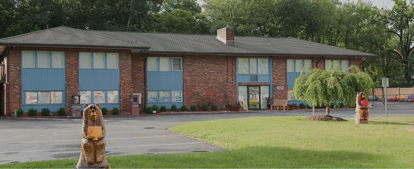 A two-story brick building with blue panels, bear statues, and a green lawn in front.