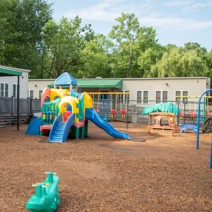 Colorful playground with slides, climbing equipment, and swings on a mulch-covered area outside.