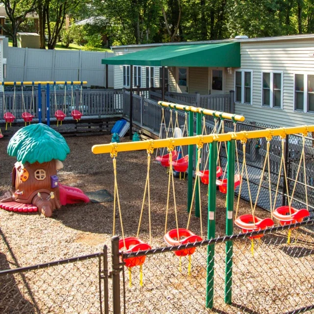 Playground with red swings, a treehouse slide, and the school building behind it on a sunny day.