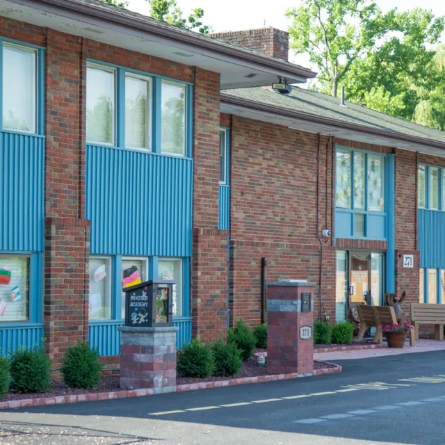 A brick two-story building with blue accents, windows, and greenery in front.