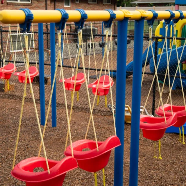 Red toddler swings hang from a blue and yellow frame at an empty playground.